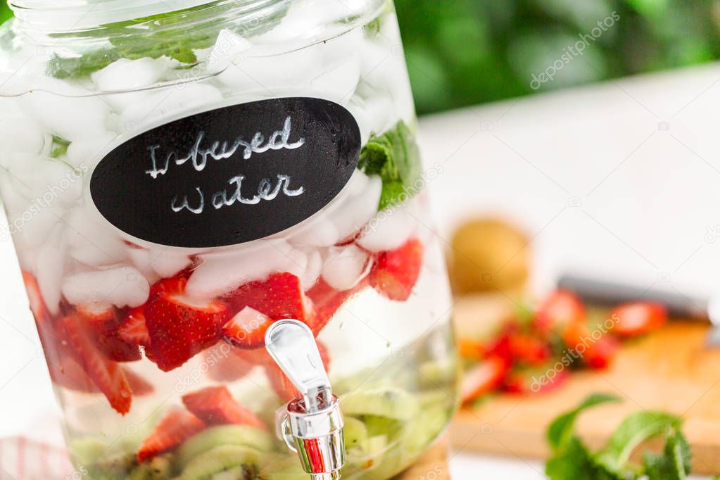 Infused water with organic strawberries, kiwi and fresh mint in glass beverage drink dispenser.