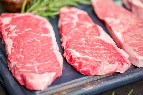 Raw New York strip steaks on a wood cutting board.