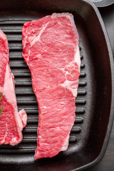 Raw New York strip steaks in cast iron frying pan.