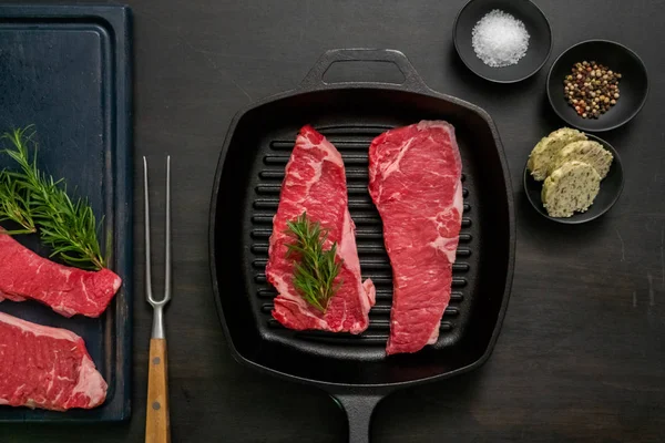 Raw New York strip steaks in cast iron frying pan.