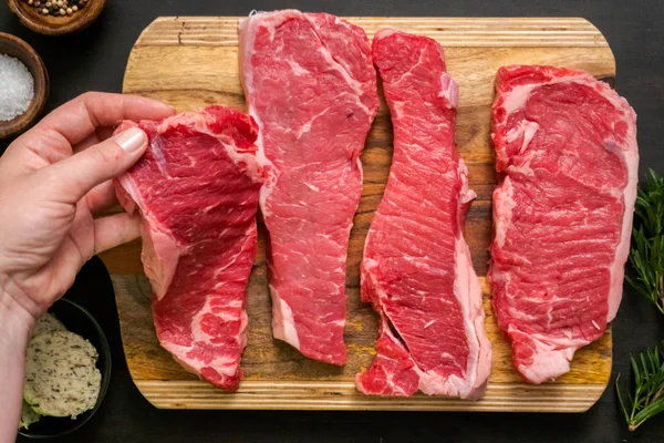 Raw New York strip steaks on a wood cutting board.