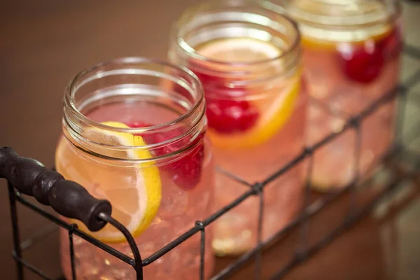 Raspberry lemonade in drinking mason jars on a wood table.