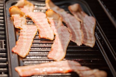 Dökme demir kalbur içinde açık gaz ızgara üzerinde ızgara domuz pastırması şeritler.