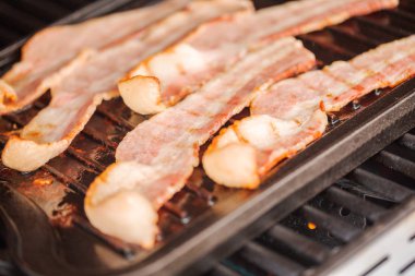 Dökme demir kalbur içinde açık gaz ızgara üzerinde ızgara domuz pastırması şeritler.