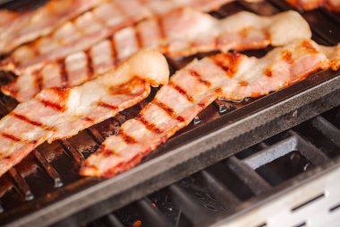 Dökme demir kalbur içinde açık gaz ızgara üzerinde ızgara domuz pastırması şeritler.