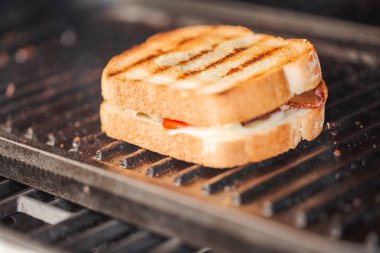 Grilling grilled cheese sandwich with bacon strips and fresh tomato on outdoor gas grill. clipart