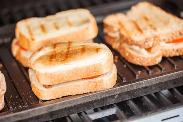 Grilling grilled cheese sandwich with bacon strips and fresh tomato on outdoor gas grill.