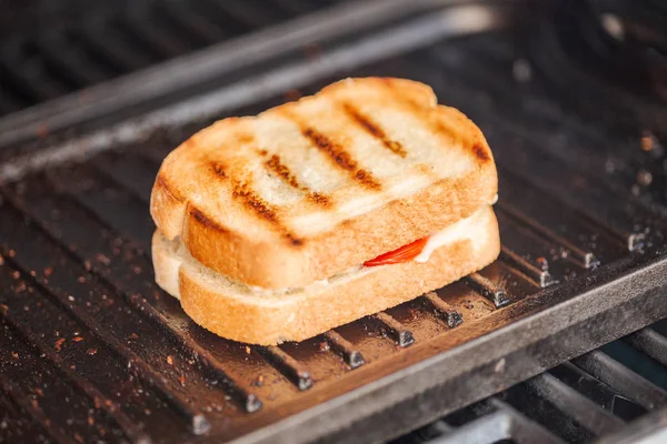 Grilling grilled cheese sandwich with bacon strips and fresh tomato on outdoor gas grill.