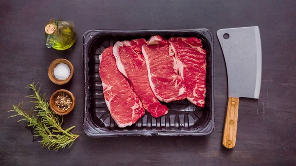 Siyah plastik et ambalaj kapsayıcısında ham New York şerit biftek.