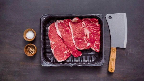 Siyah plastik et ambalaj kapsayıcısında ham New York şerit biftek.