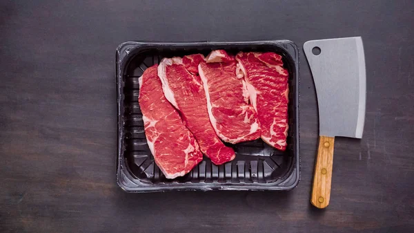 Siyah plastik et ambalaj kapsayıcısında ham New York şerit biftek.