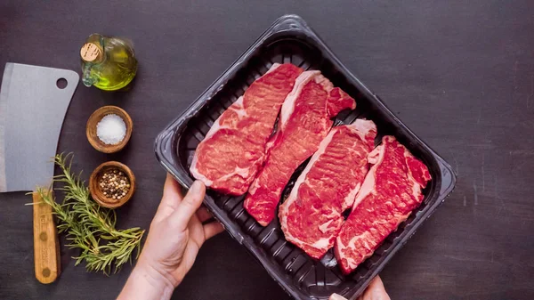 Siyah plastik et ambalaj kapsayıcısında ham New York şerit biftek.