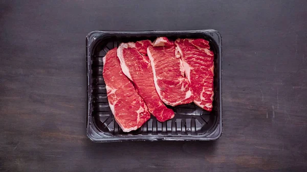 Siyah plastik et ambalaj kapsayıcısında ham New York şerit biftek.