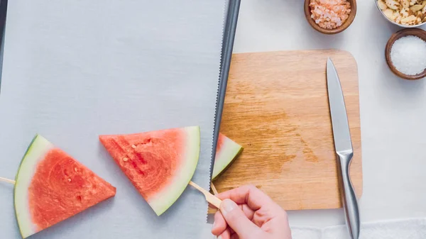 Step by step. Sliding the wood pop stick into the watermelon wage wedge to make watermelon ice pops.