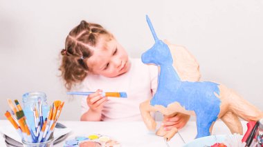 Küçük kız boyama kağıt mache unicorn mavi boya ile.