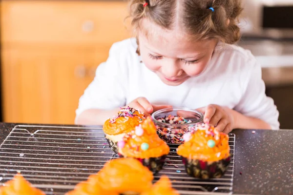 ふりかけミックスでカップケーキにアイシングとオレンジを飾る少女 — ストック写真