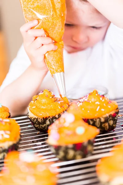 Kleines Mädchen Dekoriert Orange Sahnehäubchen Auf Cupcakes Mit Streuselmix — Stockfoto