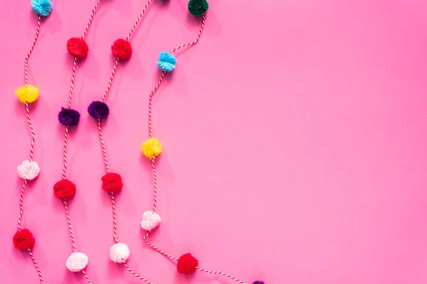 Pom pom colorful party garland on pink backgrouns.