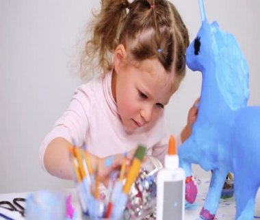 Adım adım. Küçük kız boyama kağıt mache unicorn mavi boya ile
