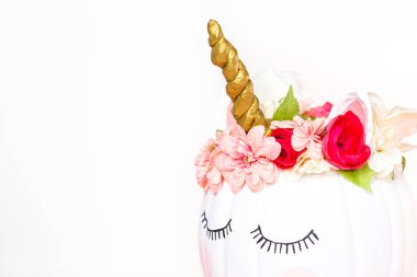 Zanaat balkabağı beyaz boyalı ve tek boynuzlu at beyaz arka plan üzerinde olarak pembe çiçeklerle süslenmiş.