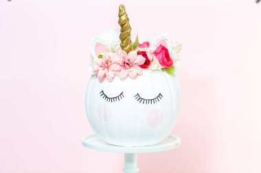 Zanaat balkabağı beyaz boyalı ve tek boynuzlu at üzerinde pembe bir arka plan olarak pembe çiçeklerle süslenmiş.