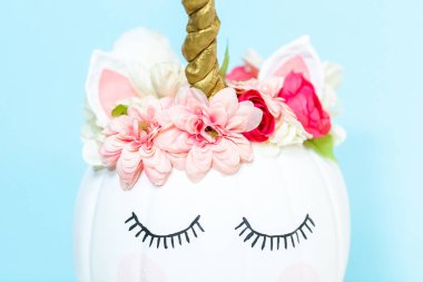 Zanaat balkabağı beyaz boyalı ve tek boynuzlu at üzerinde mavi arka plan olarak pembe çiçeklerle süslenmiş.