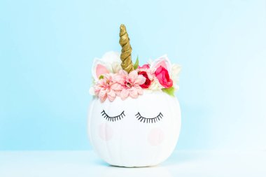 Zanaat balkabağı beyaz boyalı ve tek boynuzlu at üzerinde mavi arka plan olarak pembe çiçeklerle süslenmiş.