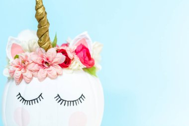 Zanaat balkabağı beyaz boyalı ve tek boynuzlu at üzerinde mavi arka plan olarak pembe çiçeklerle süslenmiş.