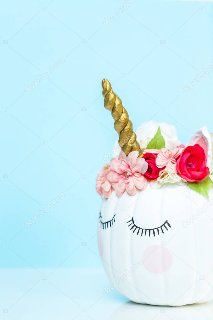 Craft pumpkin painted white and decorated with pink flowers as unicorn on blue background.