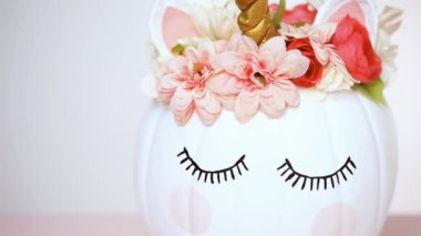 Zanaat balkabağı beyaz boyalı ve tek boynuzlu at üzerinde pembe bir arka plan olarak pembe çiçeklerle süslenmiş.