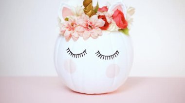 Zanaat balkabağı beyaz boyalı ve tek boynuzlu at üzerinde pembe bir arka plan olarak pembe çiçeklerle süslenmiş.