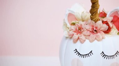 Zanaat balkabağı beyaz boyalı ve tek boynuzlu at üzerinde pembe bir arka plan olarak pembe çiçeklerle süslenmiş.