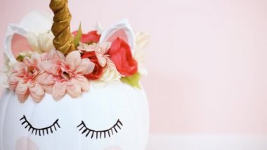 Zanaat balkabağı beyaz boyalı ve tek boynuzlu at üzerinde pembe bir arka plan olarak pembe çiçeklerle süslenmiş.