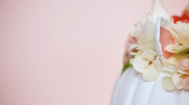 Görünümü kapatın. Zanaat balkabağı beyaz boyalı ve tek boynuzlu at üzerinde pembe bir arka plan olarak pembe çiçeklerle süslenmiş