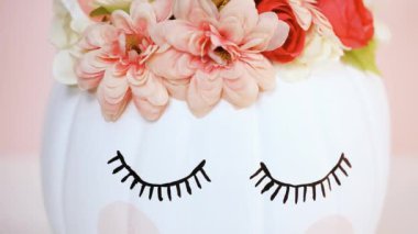 Görünümü kapatın. Zanaat balkabağı beyaz boyalı ve tek boynuzlu at üzerinde pembe bir arka plan olarak pembe çiçeklerle süslenmiş