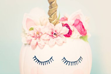 Zanaat balkabağı beyaz boyalı ve tek boynuzlu at üzerinde mavi arka plan olarak pembe çiçeklerle süslenmiş.