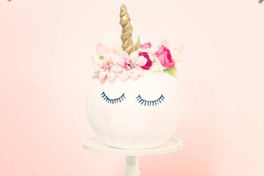 Zanaat balkabağı beyaz boyalı ve tek boynuzlu at üzerinde pembe bir arka plan olarak pembe çiçeklerle süslenmiş.