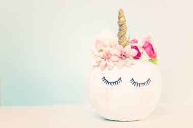 Zanaat balkabağı beyaz boyalı ve tek boynuzlu at üzerinde mavi arka plan olarak pembe çiçeklerle süslenmiş.