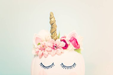 Zanaat balkabağı beyaz boyalı ve tek boynuzlu at üzerinde mavi arka plan olarak pembe çiçeklerle süslenmiş.