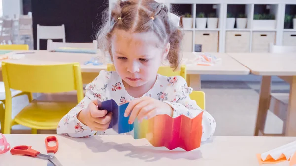 Little girl making paper butterflies from multicolor paper.