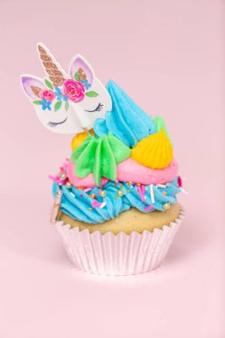 Tek boynuzlu at çok renkli buttercream buzlanma ve tek boynuzlu at cupcake topper üzerinde pembe bir arka plan ile cupcakes fantezi.