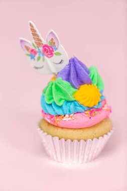 Tek boynuzlu at çok renkli buttercream buzlanma ve tek boynuzlu at cupcake topper üzerinde pembe bir arka plan ile cupcakes fantezi.