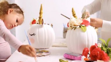 Anne ve kızı yüzü bir tek boynuzlu at boyama ve zanaat kabak çiçekleri ile dekorasyon tema kabak Cadılar Bayramı için bir tek boynuzlu at yapmak