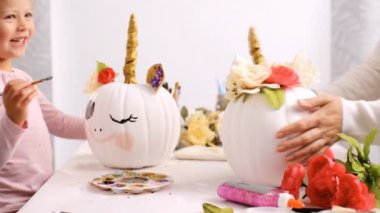 Anne ve kızı yüzü bir tek boynuzlu at boyama ve zanaat kabak çiçekleri ile dekorasyon tema kabak Cadılar Bayramı için bir tek boynuzlu at yapmak