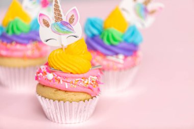 Tek boynuzlu at çok renkli buttercream buzlanma ve tek boynuzlu at cupcake topper üzerinde pembe bir arka plan ile cupcakes fantezi.