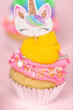 Tek boynuzlu at çok renkli buttercream buzlanma ve tek boynuzlu at cupcake topper üzerinde pembe bir arka plan ile cupcakes fantezi.