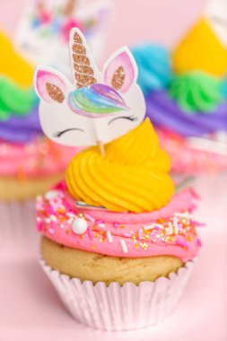 Tek boynuzlu at çok renkli buttercream buzlanma ve tek boynuzlu at cupcake topper üzerinde pembe bir arka plan ile cupcakes fantezi.