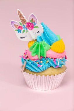 Tek boynuzlu at çok renkli buttercream buzlanma ve tek boynuzlu at cupcake topper üzerinde pembe bir arka plan ile cupcakes fantezi.