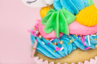 Tek boynuzlu at çok renkli buttercream buzlanma ve tek boynuzlu at cupcake topper üzerinde pembe bir arka plan ile cupcakes fantezi.