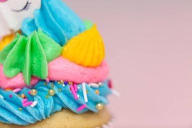 Tek boynuzlu at çok renkli buttercream buzlanma ve tek boynuzlu at cupcake topper üzerinde pembe bir arka plan ile cupcakes fantezi.